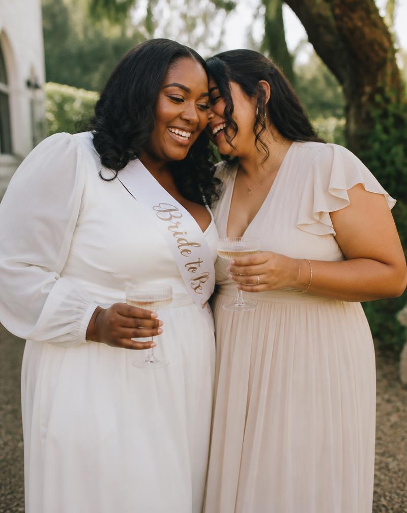 Two brides celebrating, one wearing a sash